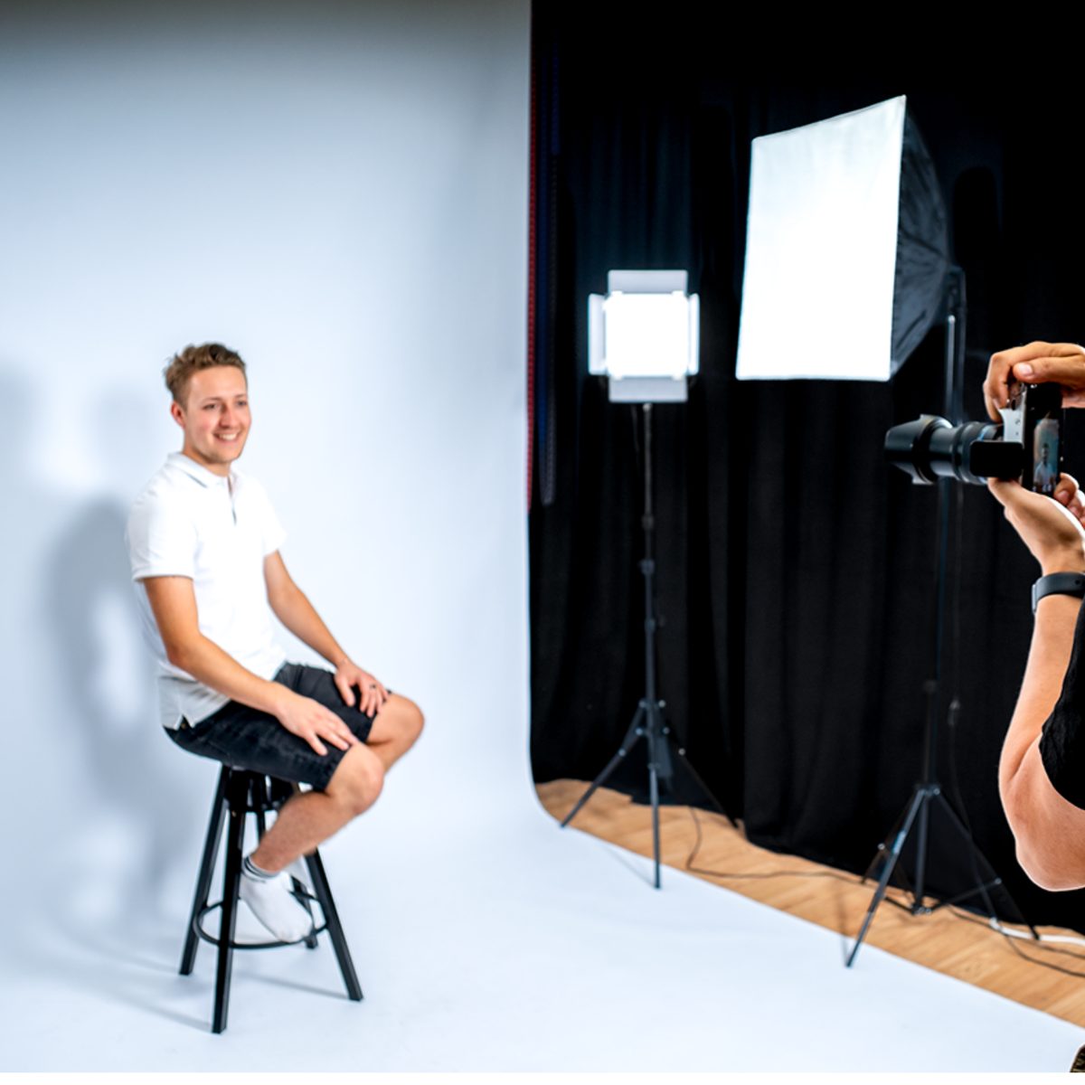 Passfoto-Aufnahme im Fotostudio Peuerbach: Kunde auf dem Hocker vor weißem Hintergrund, professionelle Studiobeleuchtung, Fotograf mit Kamera